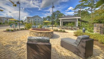 Poolside fire pit with oversized chairs, outdoor grilling station, and tables at Lullwater at Blair Stone apartments for rent in Tallahassee, FL